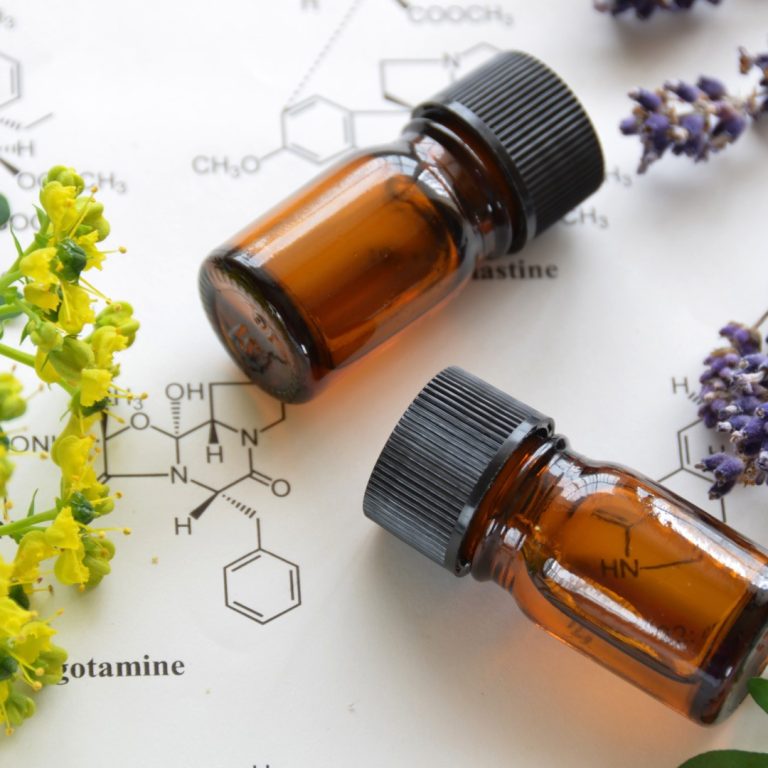 bouteille d'huile essentielle posée sur une table avec dessins de molécules et fleur de lavande